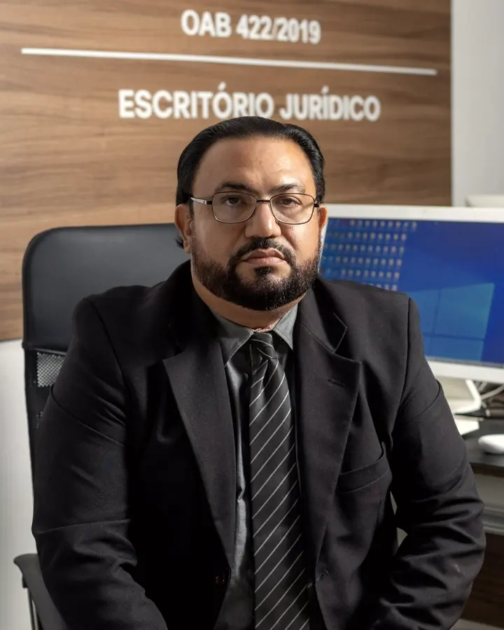 Glaucio H. Alencar sentado à mesa, sob a placa do escritório jurídico