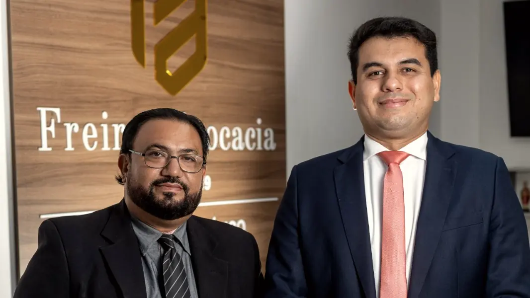 Glaucio H. Alencar e Linconl Freire lado a lado, sorrindo, diante da placa do escritório
